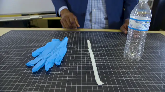 A rubber glove, a drinking straw and a water bottle on a cutting mat.