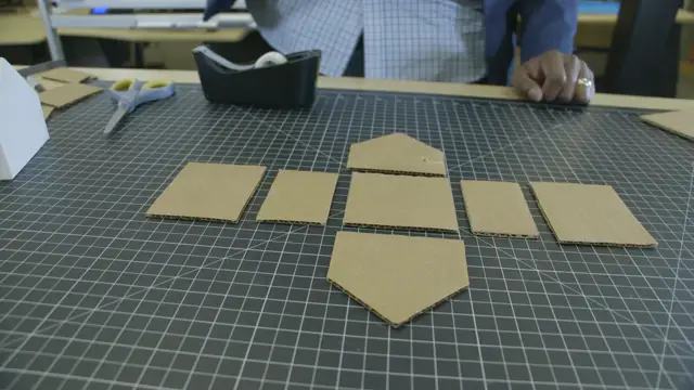 Cardboard walls and roof pieces cut and laid out flat on a cutting mat, with scissors and tape behind them.