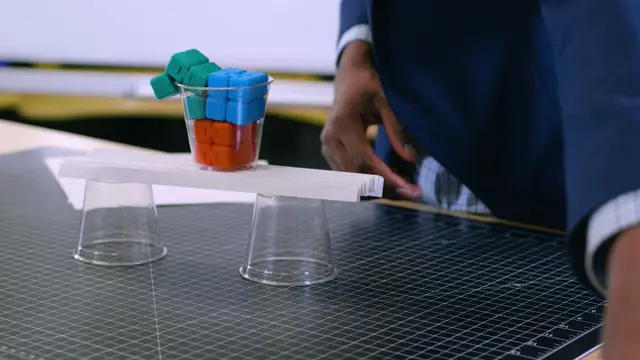 A cup full of toy blocks resting on a sheet of paper folded in zigzags across two cups.