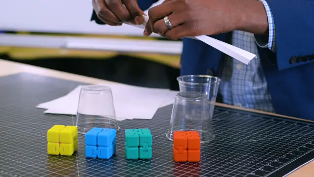 A sheet of paper resting across two plastic cups, with colorful toy blocks ready as weights.