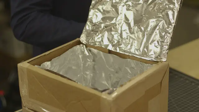 A cardboard box lined with aluminum foil, its foil-covered flap raised to reflect the sun inside.
