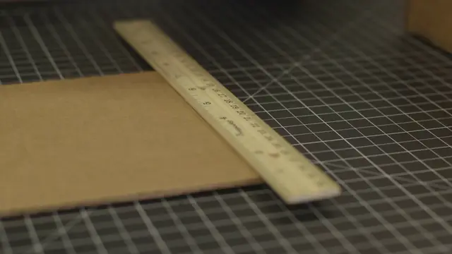 A wooden ruler laid across a piece of cardboard on a cutting mat, ready to mark a stick.