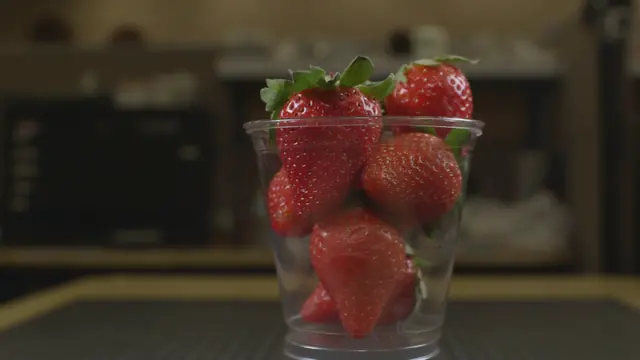 Fresh strawberries in a clear plastic cup on a cutting mat.